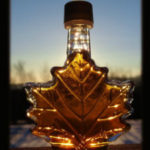 A clear bottle in the shape of a maple leaf filled with maple syrup