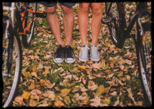 A man and a woman's legs and feet with tennis shoes standing in a wooded area with bikes next to each person