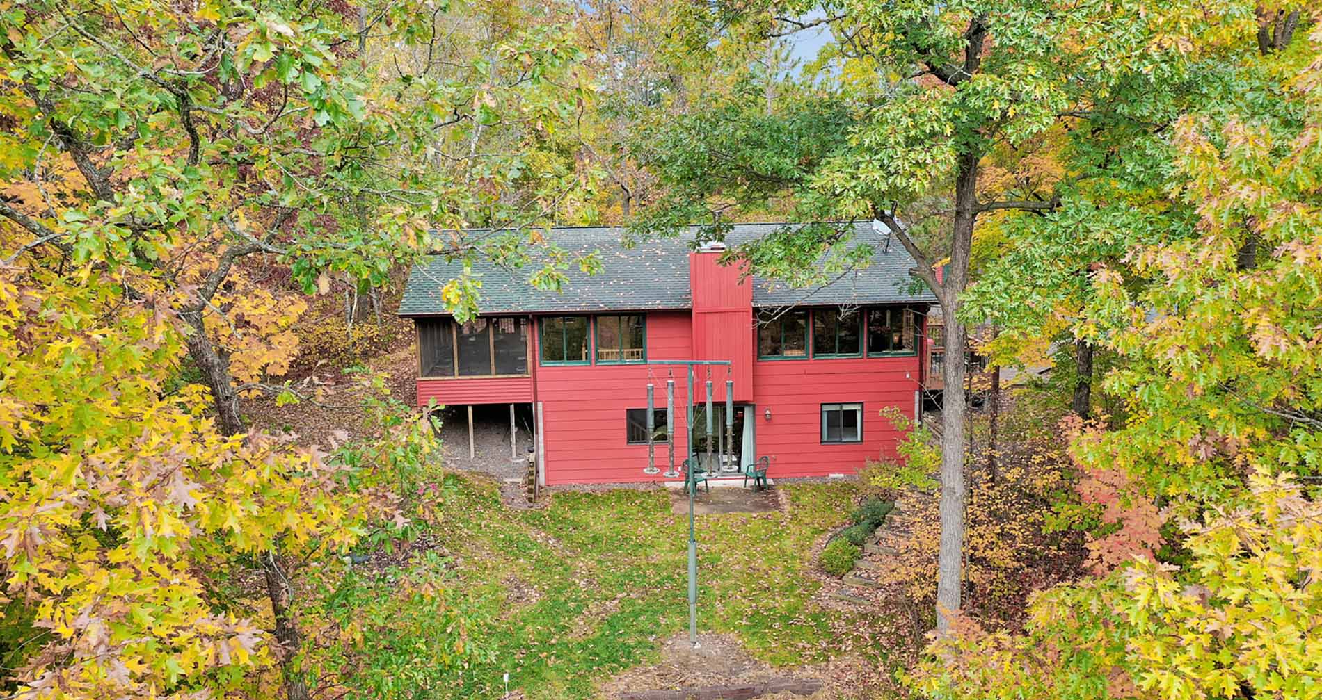 Exterior view, through the trees, of the 2 story red cabin with full screened in porch